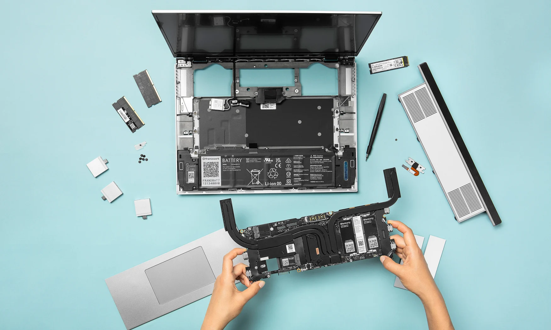 Photo marketing pour Framework Laptop 16, montrant une vue de dessus d'une personne échangeant des pièces. Ordinateur portable partiellement démonté avec des morceaux partout. Deux mains sortant du bas du cadre tiennent une unité, y compris la mémoire et les graphiques.